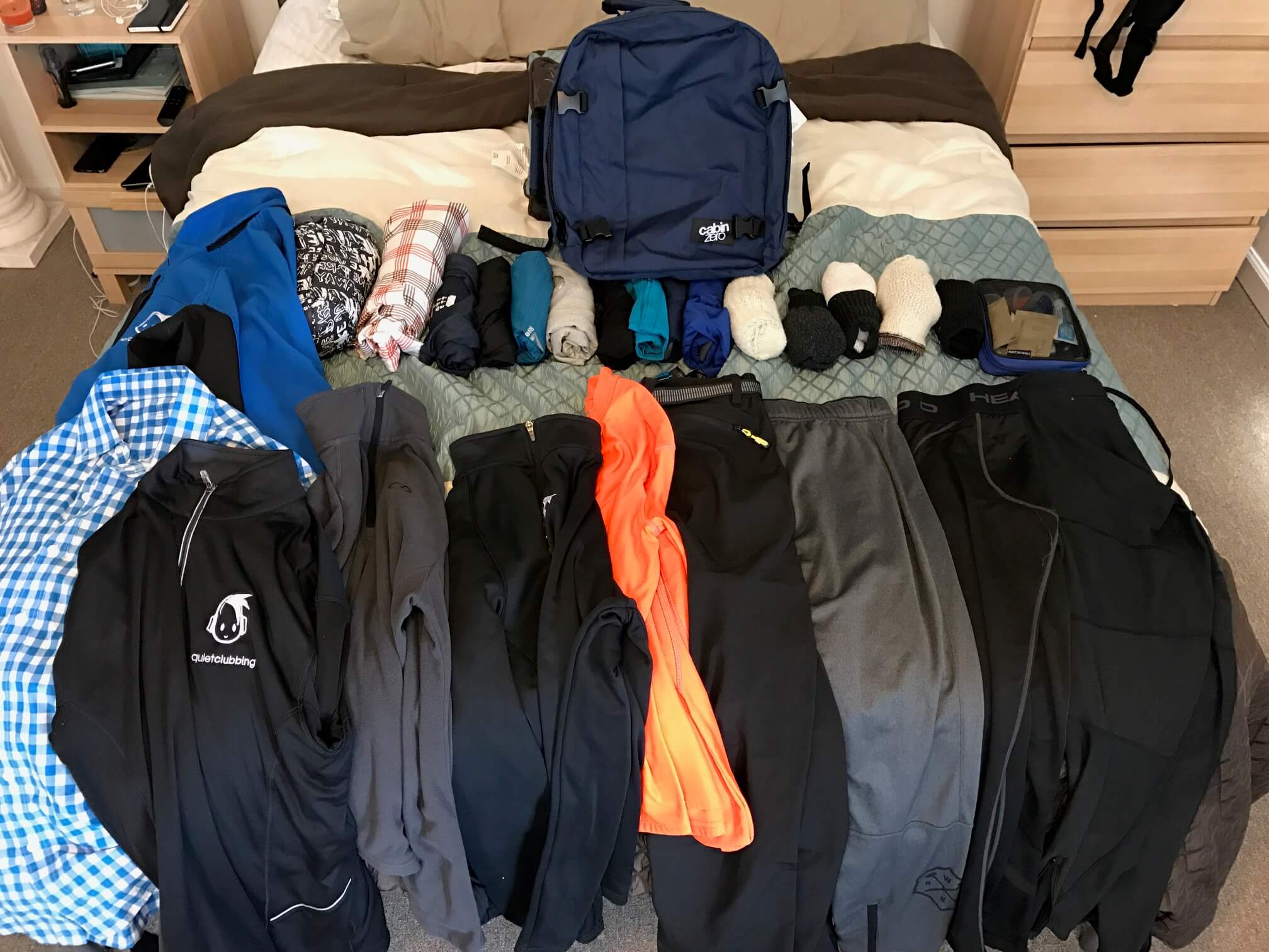 Clothes and luggage items laid out on a bed to show you the best Backpack to avoid luggage fees