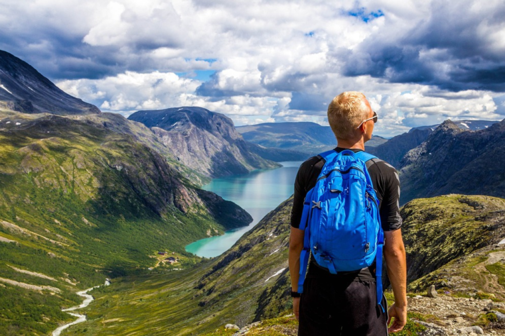 Man looking out into a valley wearing a bright blue backpack which is the only backpack to avoid luggage fees