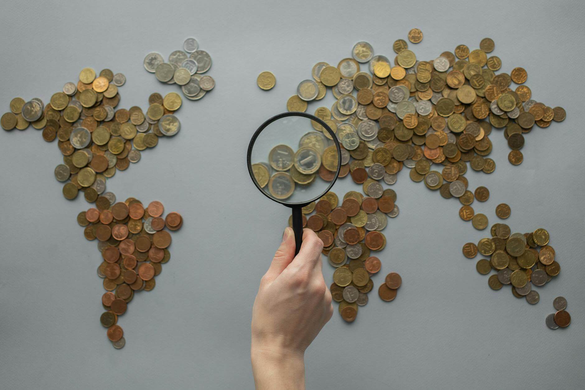 anonymous person with magnifying glass over world map of coins showing you how to handle money while traveling 