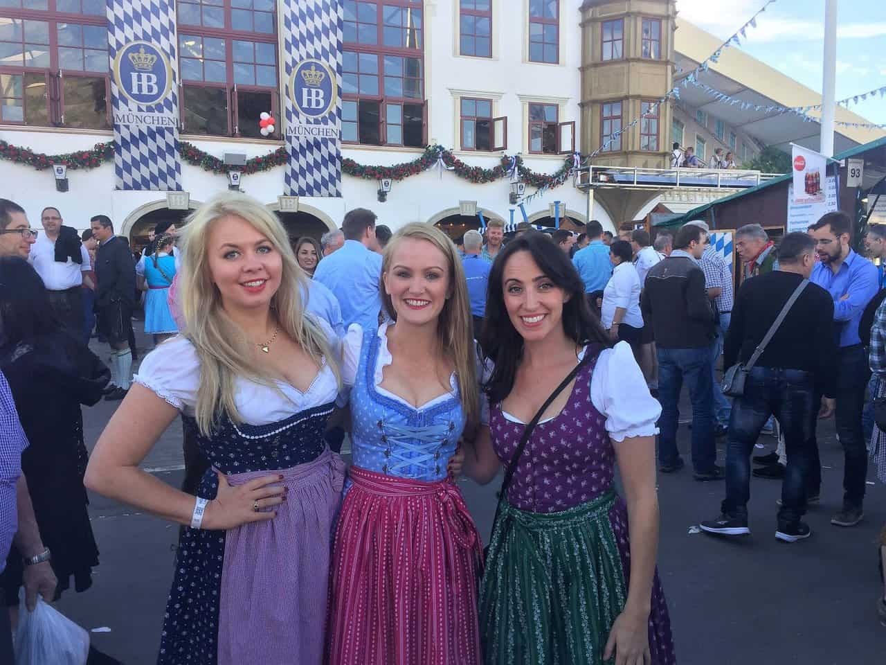 Women in Traditional Dirndls at Hofbräuhaus Oktoberfest Three women dressed in colorful dirndls posing outside Hofbräuhaus tent during Oktoberfest in Munich