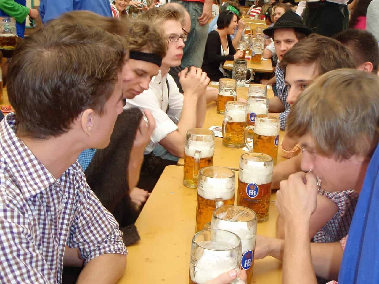 Group of Men Drinking Beer at Oktoberfest Hofbräuhaus Tent Young men seated at long wooden tables with large beer mugs during Oktoberfest celebration
