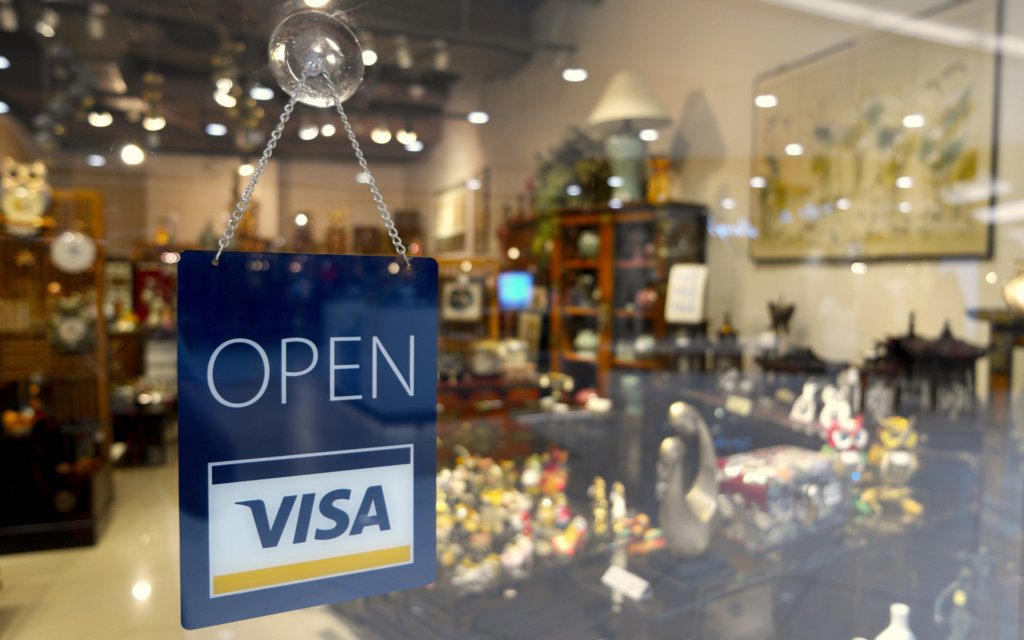 A sign hanging outside a store that says Open and Visa