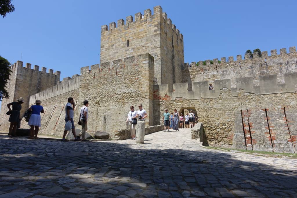 Tourists walking around the stone walls and entrance of the medieval São Jorge Castle in Lisbon