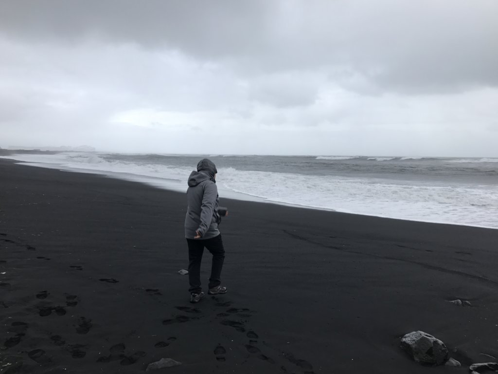 Man walking on black sand by the water 