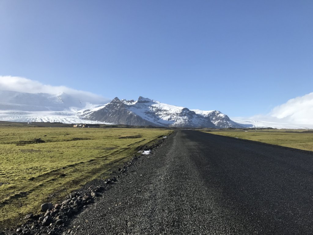 An unpaved road leading towards white capped mountains in Iceland