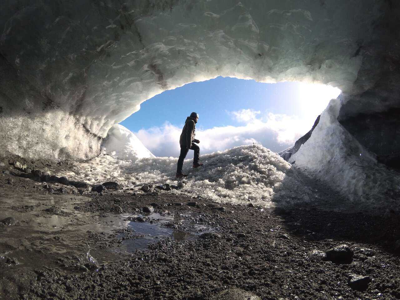 Man standing inside a stunning blue ice cave, surrounded by translucent ice walls in Iceland.
