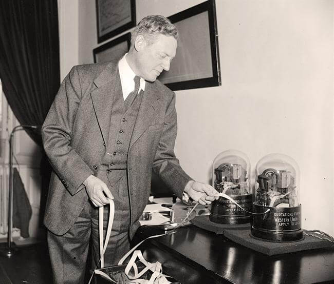 Black and White photo of Man pulling paper from a ticker tape machine