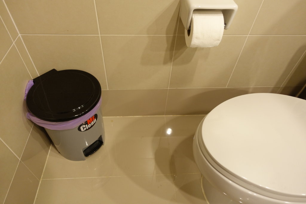 A small garbage can that you can open with your foot, near a toilet