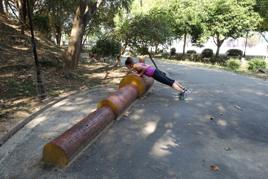 woman doing a pushup on a log in a park 