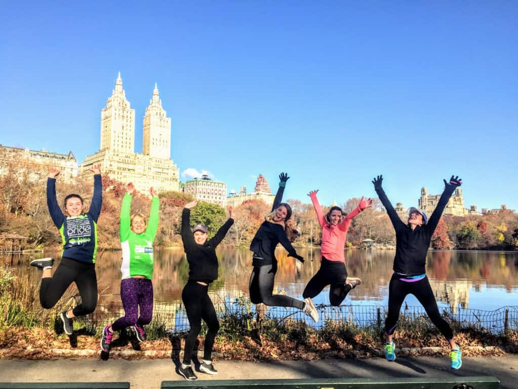 Six woman in winter running gear jumping in front of a lake