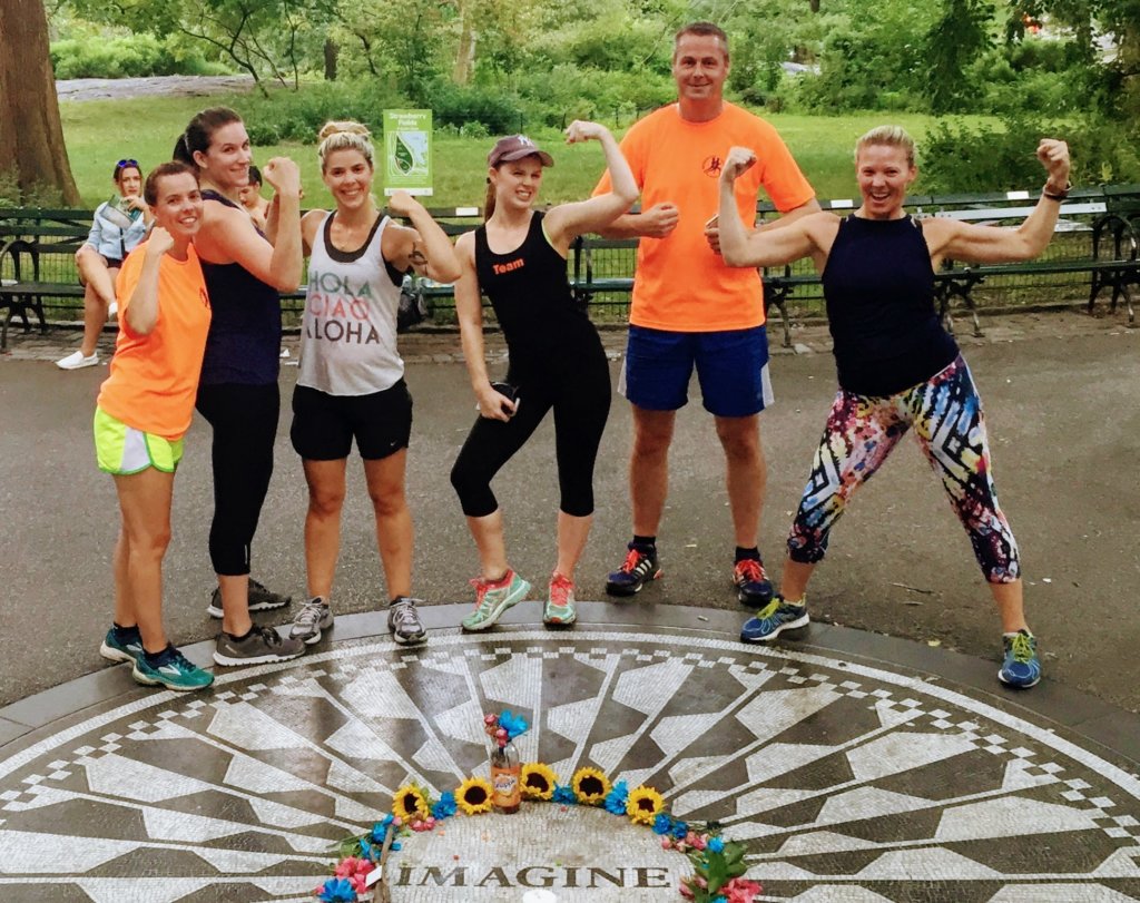 A group of people in running gear making muscles in front of the imagine circle in central park