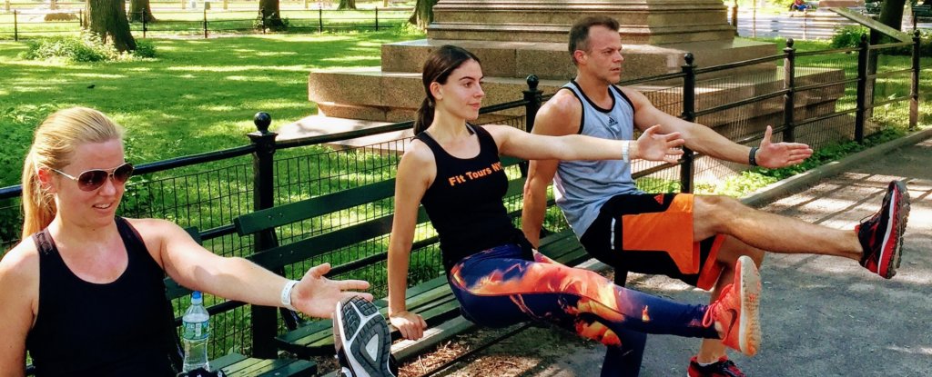 Three people doing a pistol sqaut on the bench in central park