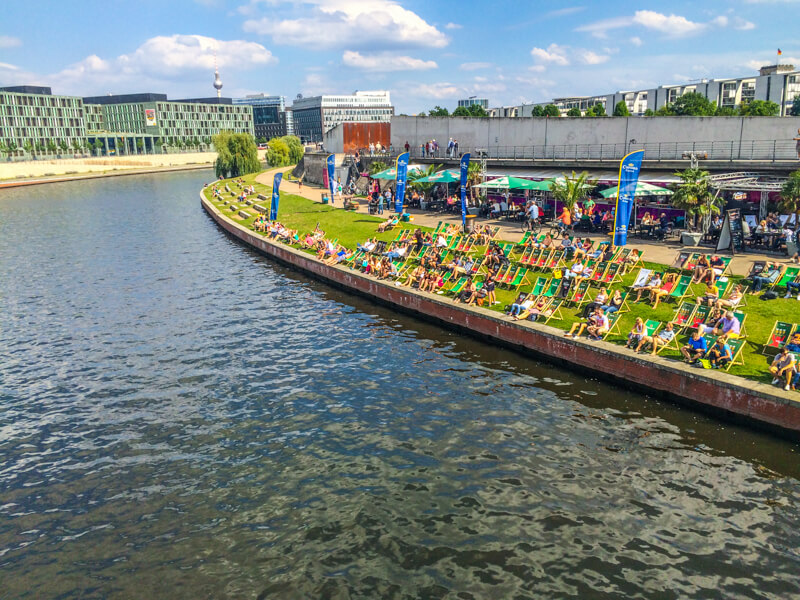 A view from a boat crusing down the Berlin river of people lounging 