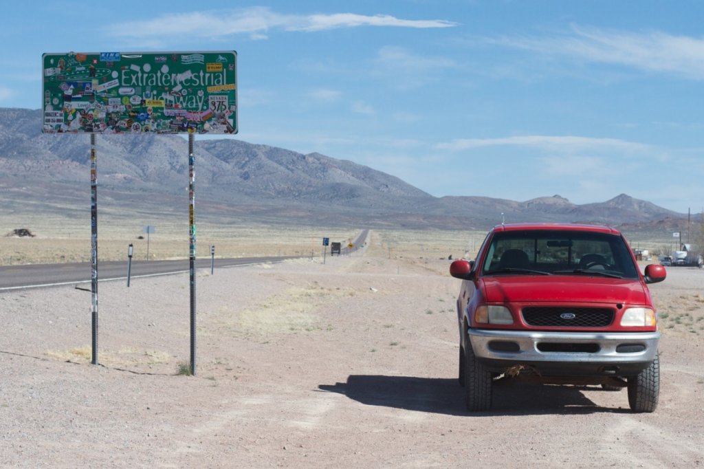 A red pick up truck driving past a road sign with mountains in the background