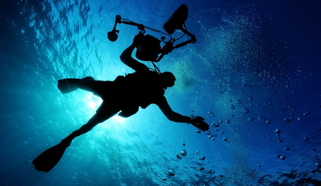 A person under water with a large camera floating above