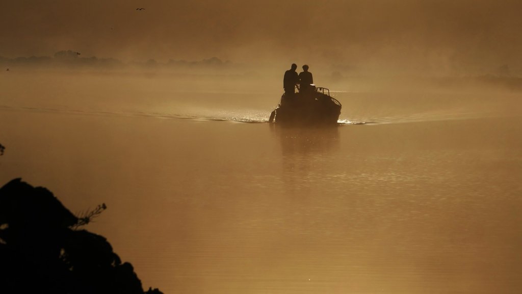 Two people in a small boat on a lake with a cloudy, smokey covering to make it look spooky 