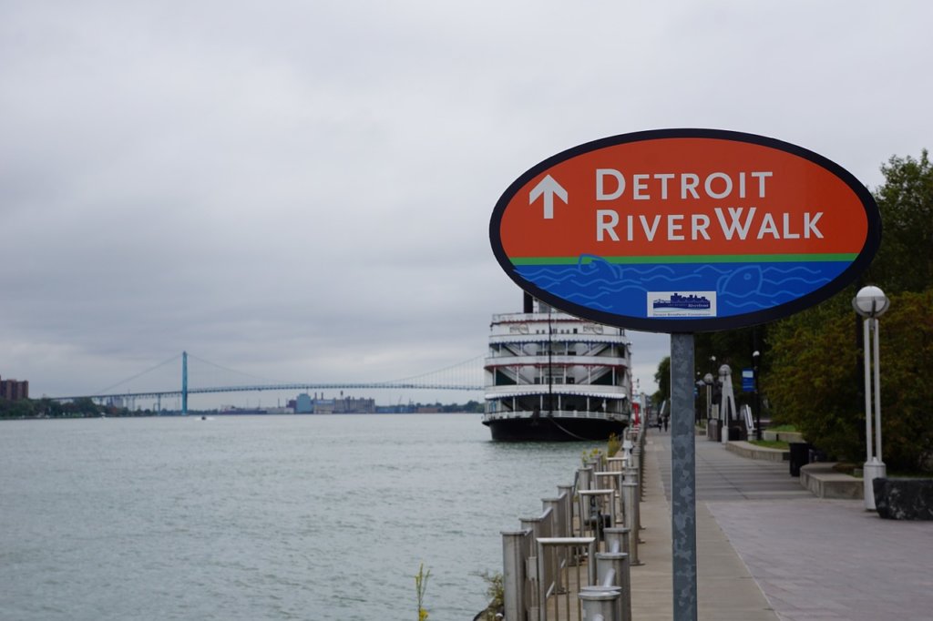 A red and blue sign along the waterway that says Detroit Riverwalk to try unique foods in michigan 