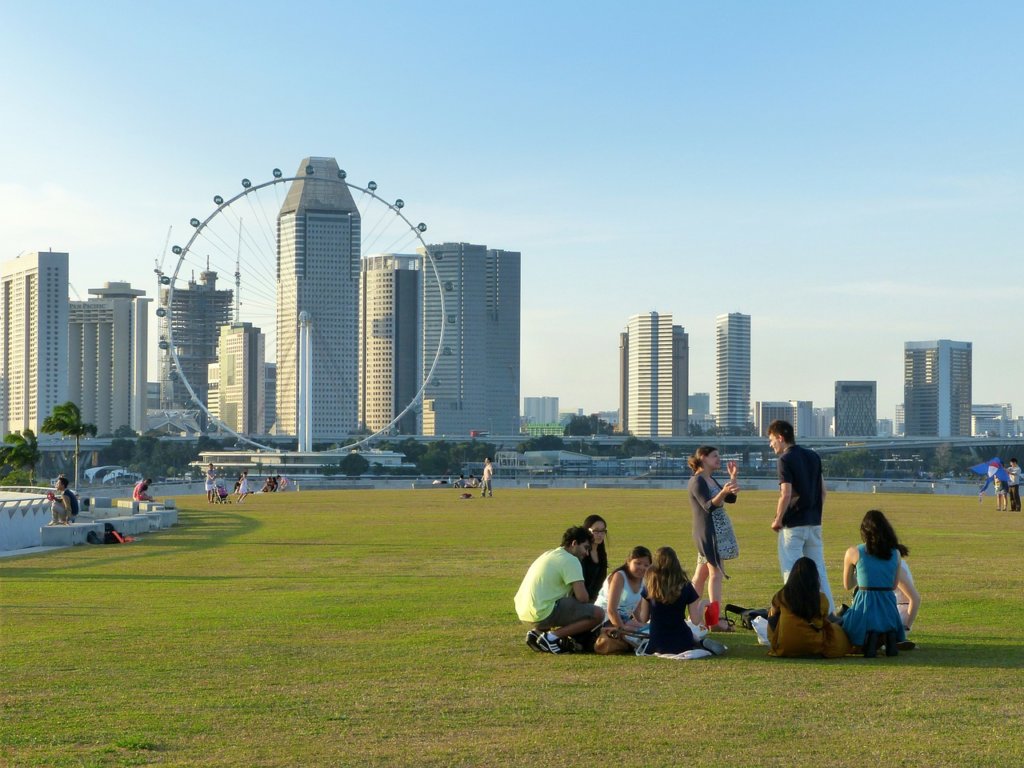 A very clean park with people sitting on the grass looking at the skyline