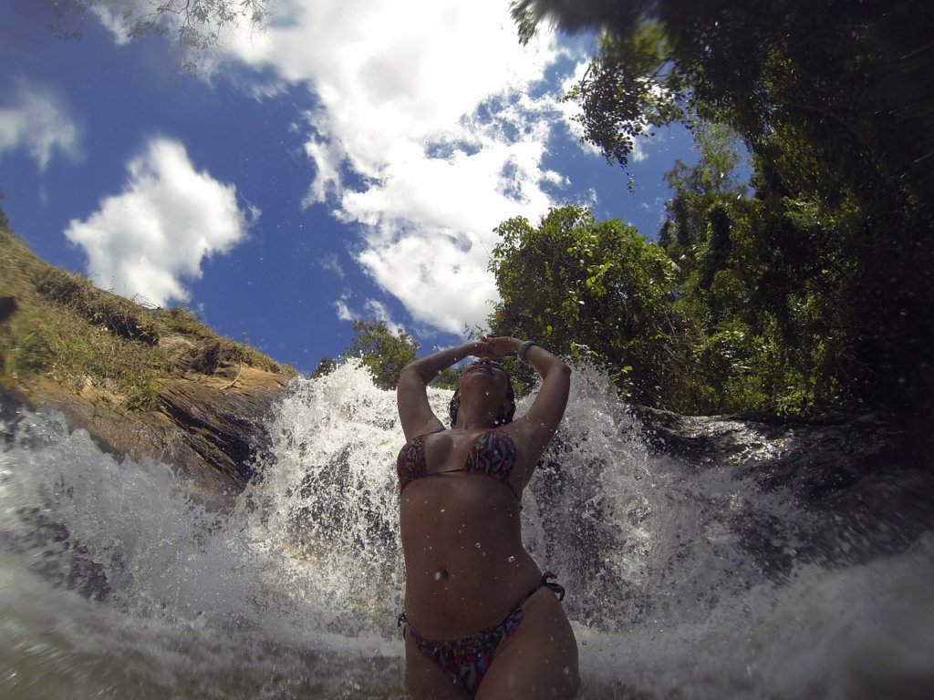 A woman in a bikini with her arms up in front of a waterfall 