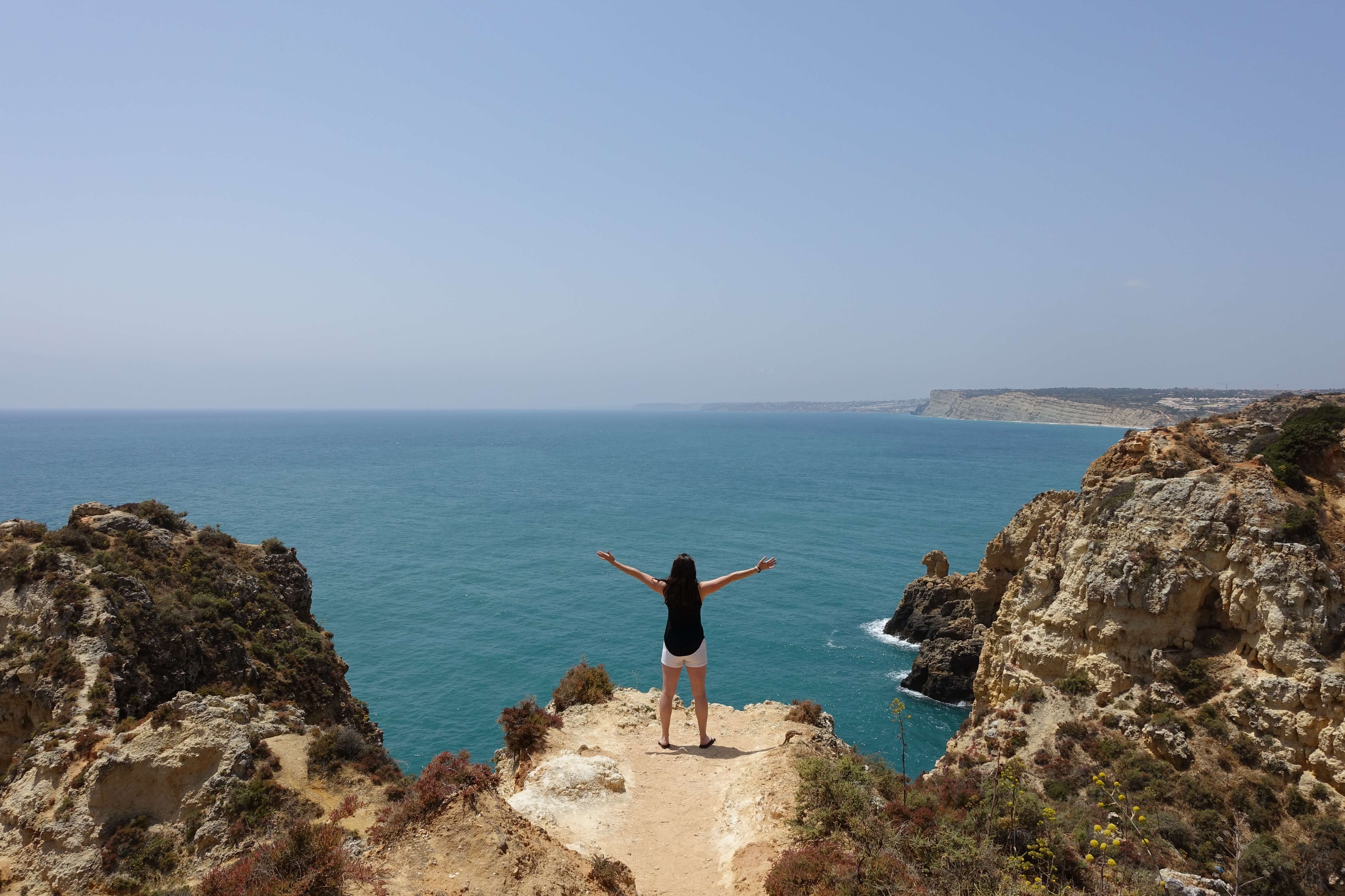 A woman standing at a cliff looking at blue water
