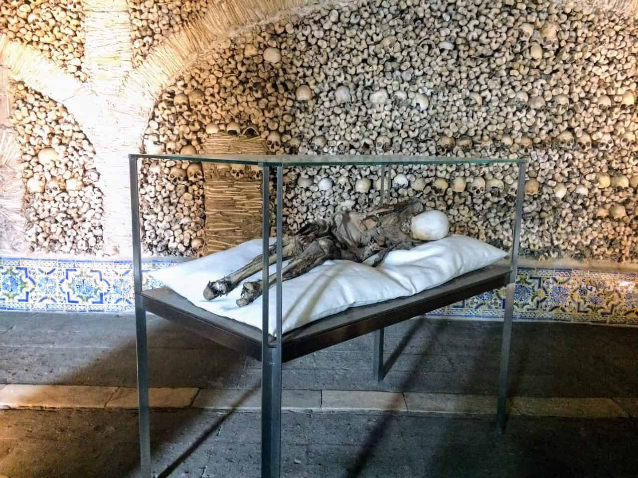 A glass case with bones inside of it on a pillow at the Evora bone chapel