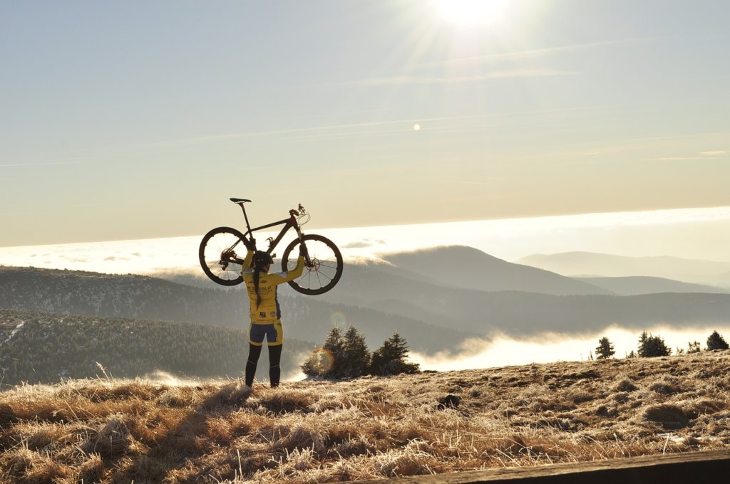 A man holding a bike up in the air looking at snow capped mountains