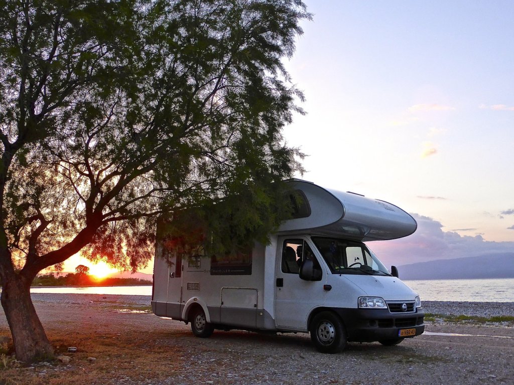 A white motorhome, or known in the UK as a british caravan, on a beach with a sunset 