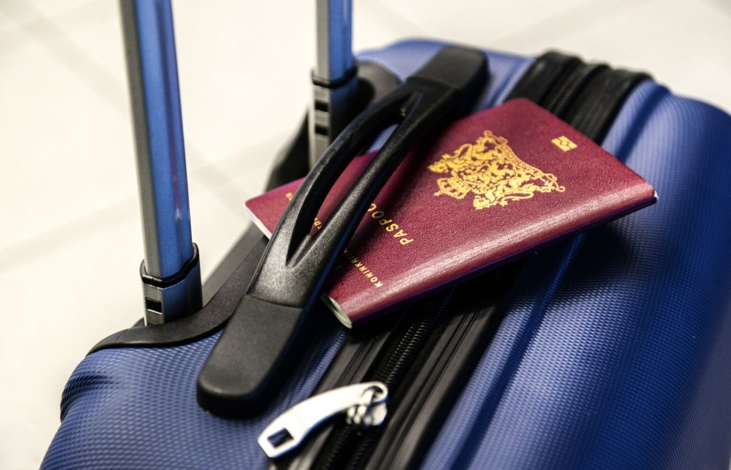 A blue suitcase with a brown passport on top near the handle