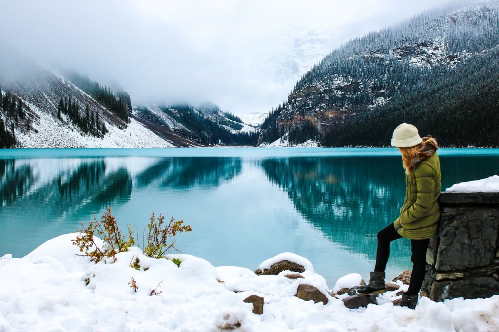 A woman standing next to a snow covered lake and mountains as an example of a RV fitness destinations