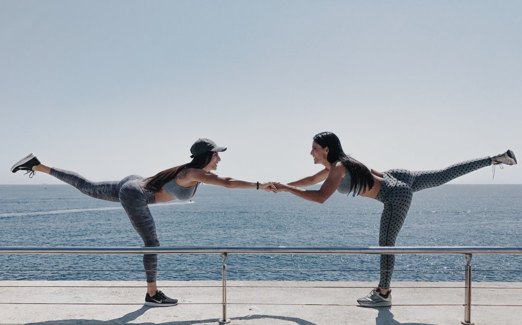Two woman holding hands with their legs in the air to motivate yourself to get fit