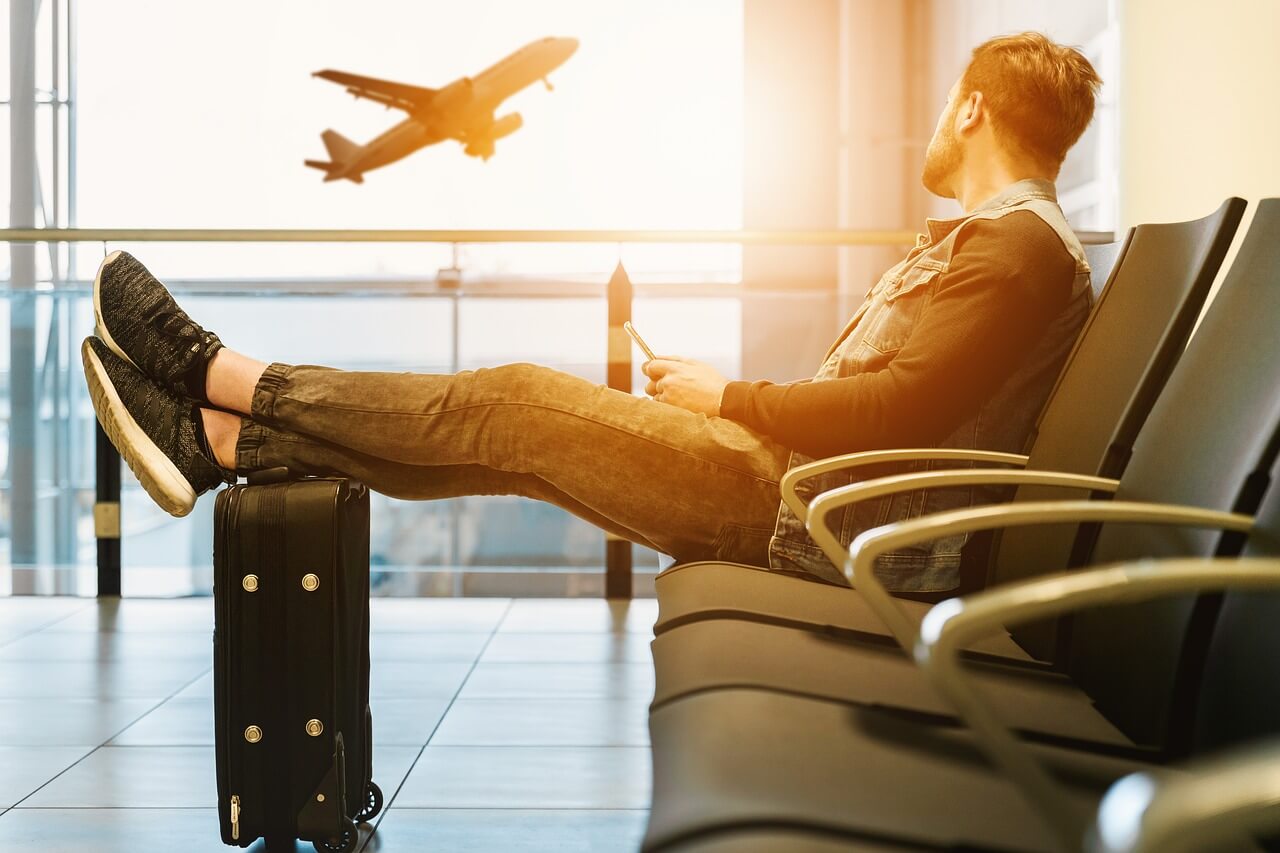 A man in an aiport sitting, watching a flight take off