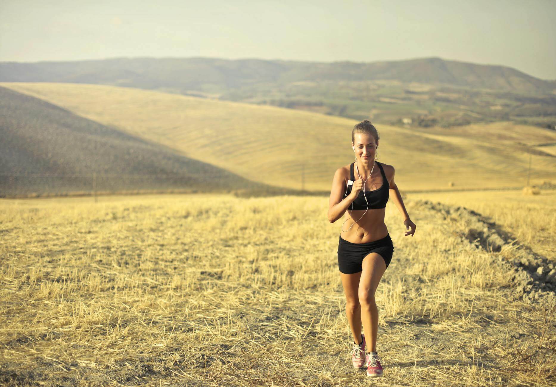 cheerful sportswoman running along hill in summer staying fit while traveling 
