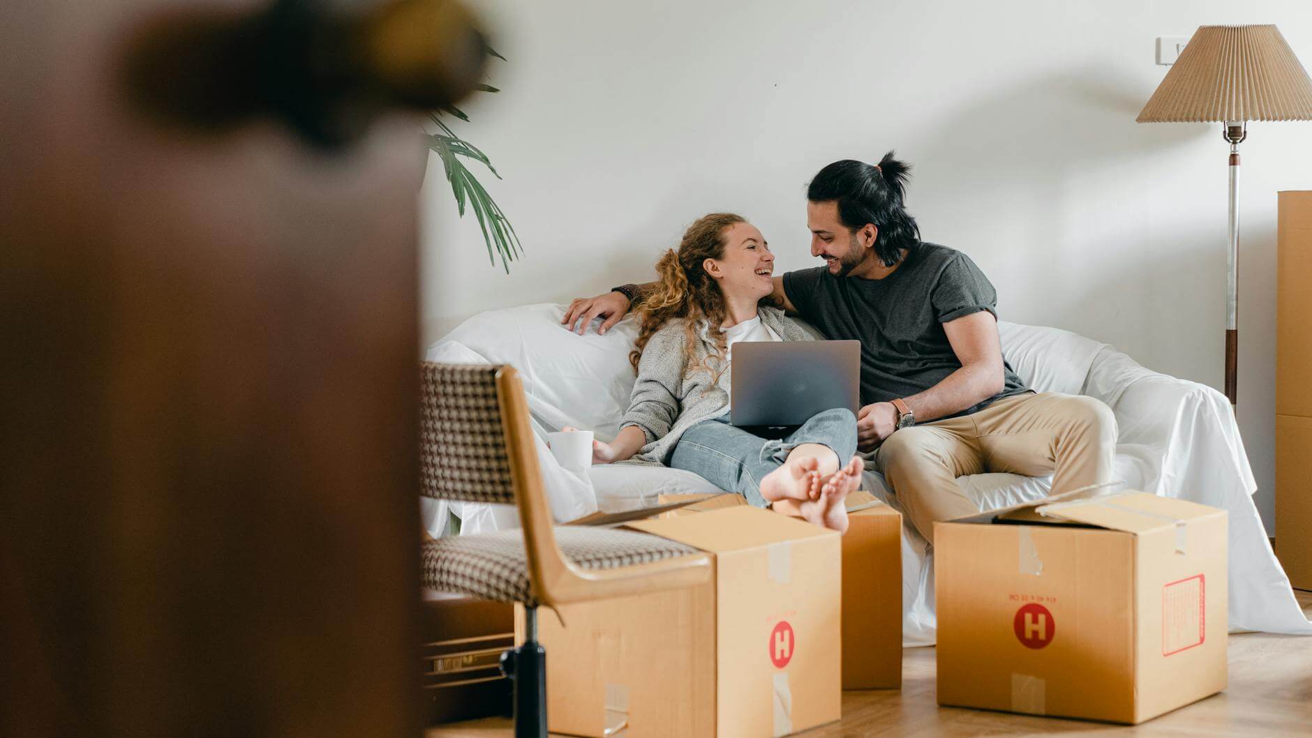 happy couple with laptop sitting on couch in new house