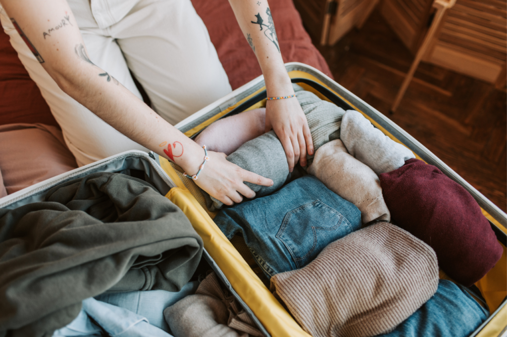 Woman rolling clothes and her essential travel items to fit into a suitcase