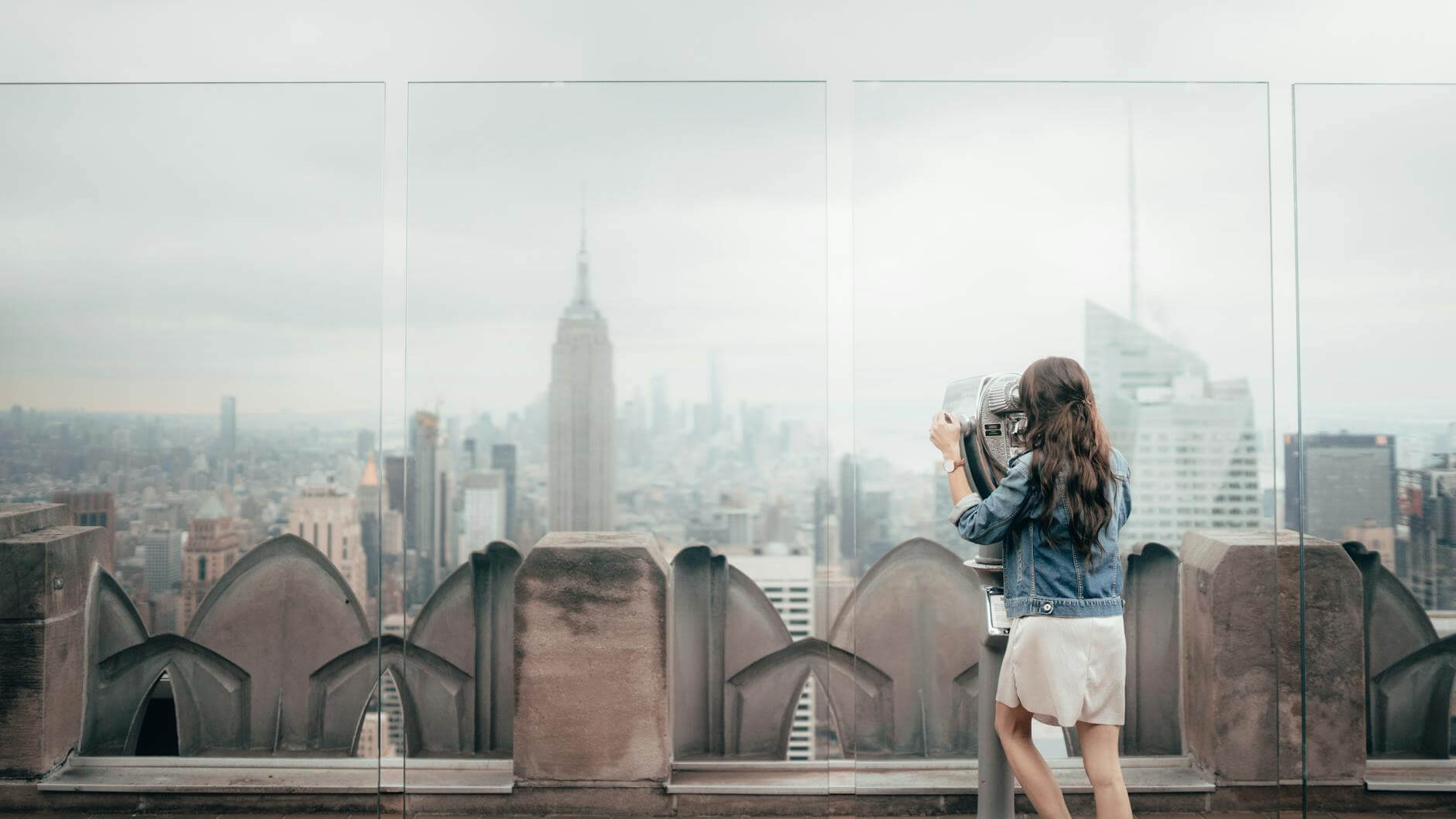 woman in blue denim jacket standing on top of building in NYC for a city break 