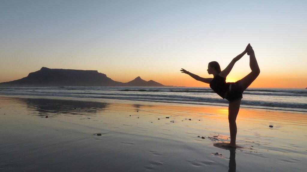 woman doing yoga at sunset on the beach showing you how to exercise while traveling