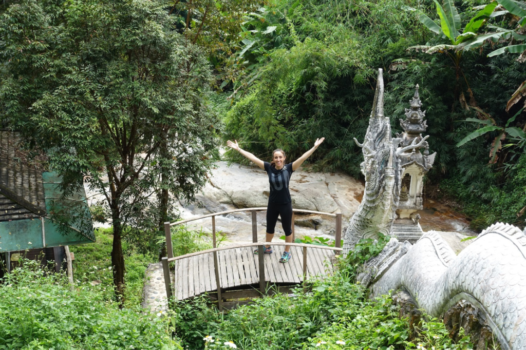 woman standing on a bridge surrounding by lush trees in thailand