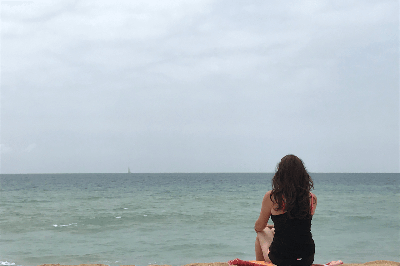 woman sitting on the beach meditating practicing one of her wellness travel tips