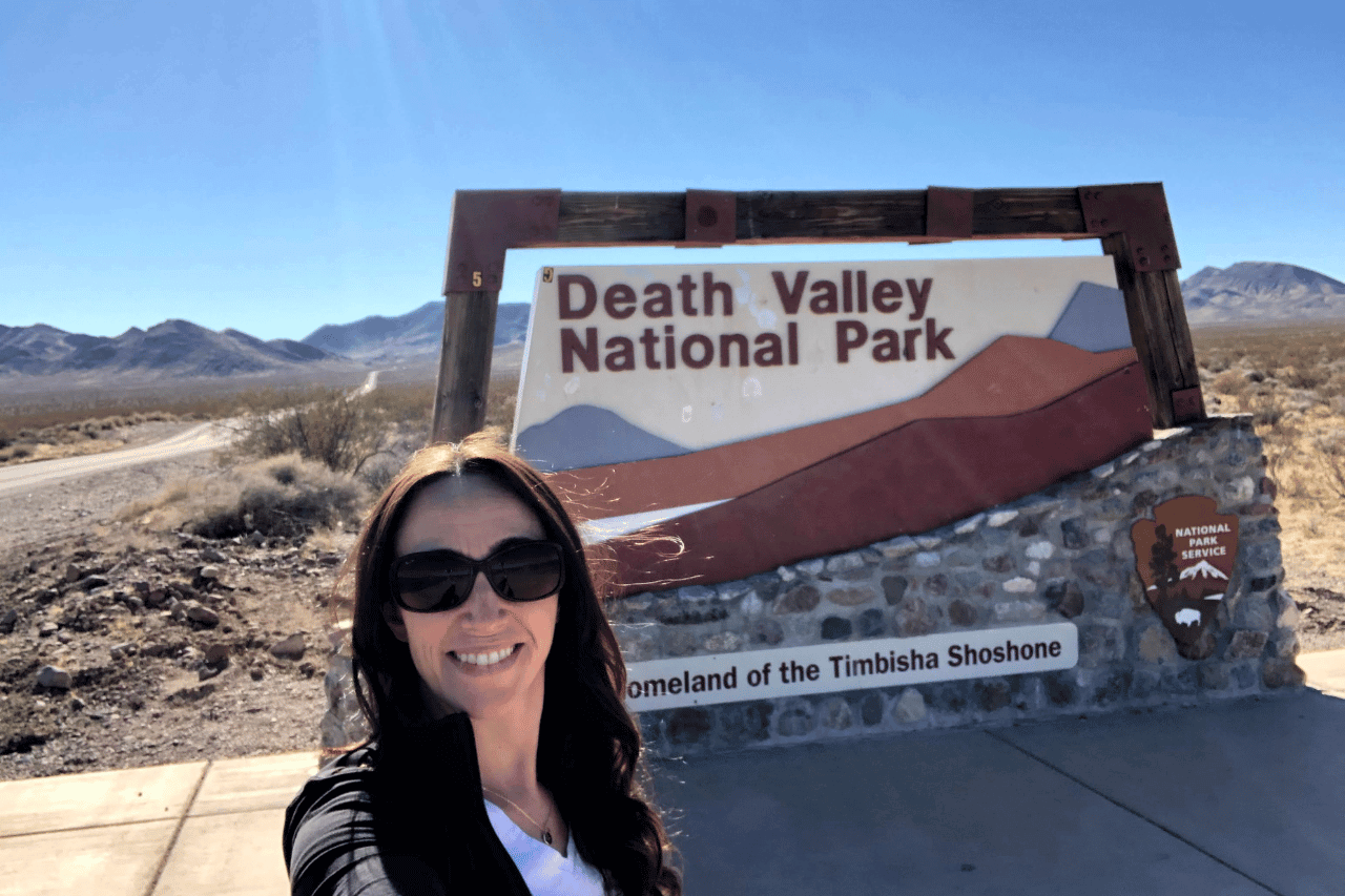 woman in front a sign for a park before hiking in death valley