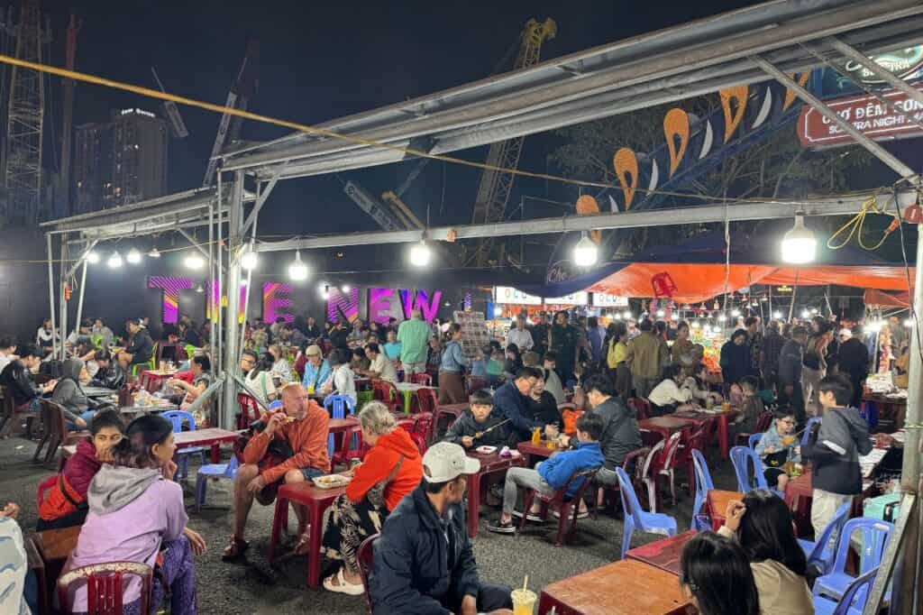 Crowds of locals and tourists eating under lights at Son Tra Night Market with Da Nang bridge sign nearby