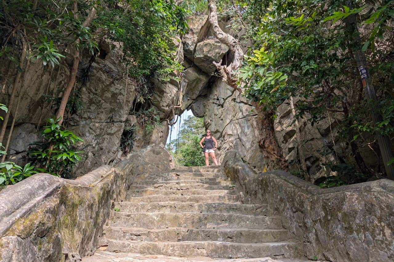 Staircase Through Natural Rock Arch Tourist standing under a dramatic natural rock arch along stone stairs at Marble Mountains Vietnam