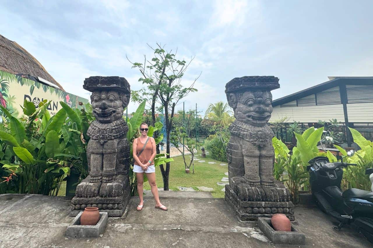 Entrance to Garden Area Near Bali Canggu Hotels with Stone Guardian Statues Tourist standing between two large stone guardian statues at a garden near Bali Canggu hotels.