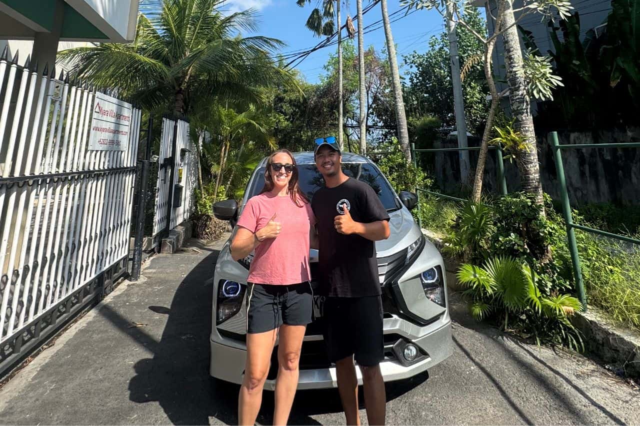 Tourist posing with a local driver in front of a silver car on a sunny day in Bali.
