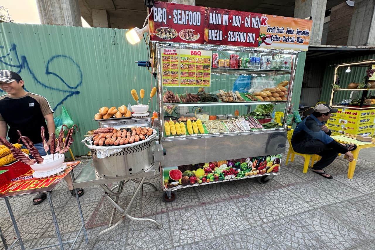 Vietnamese street food cart near My Khe Da Nang Beach selling BBQ, corn, and bread