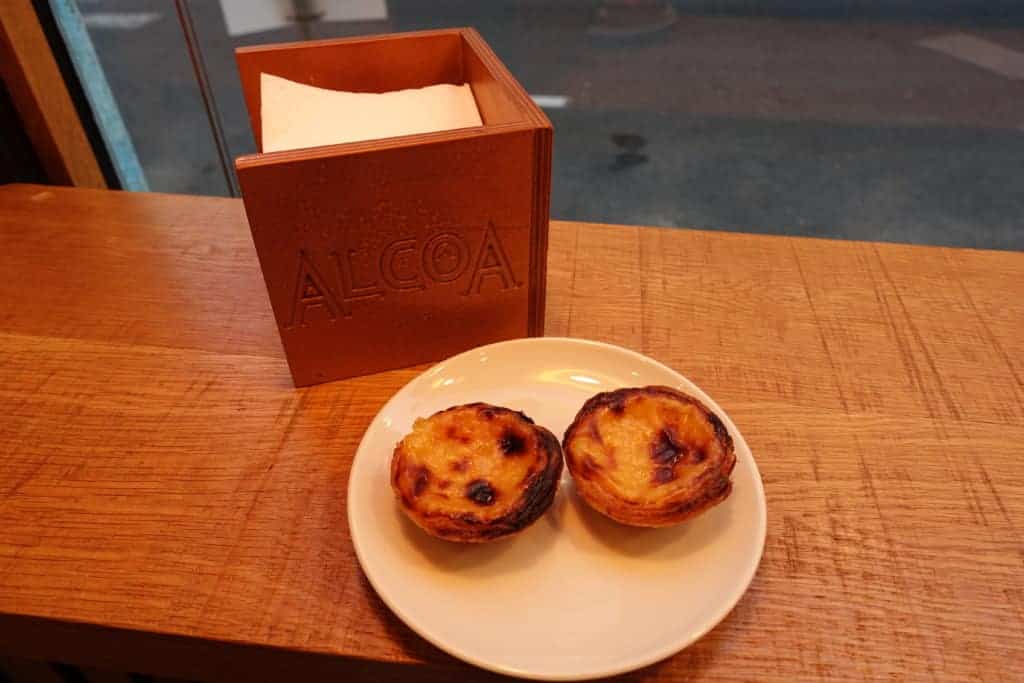 Two traditional Portuguese custard tarts (pastéis de nata) on a white plate, served at Alcoa pastry shop in Lisbon
