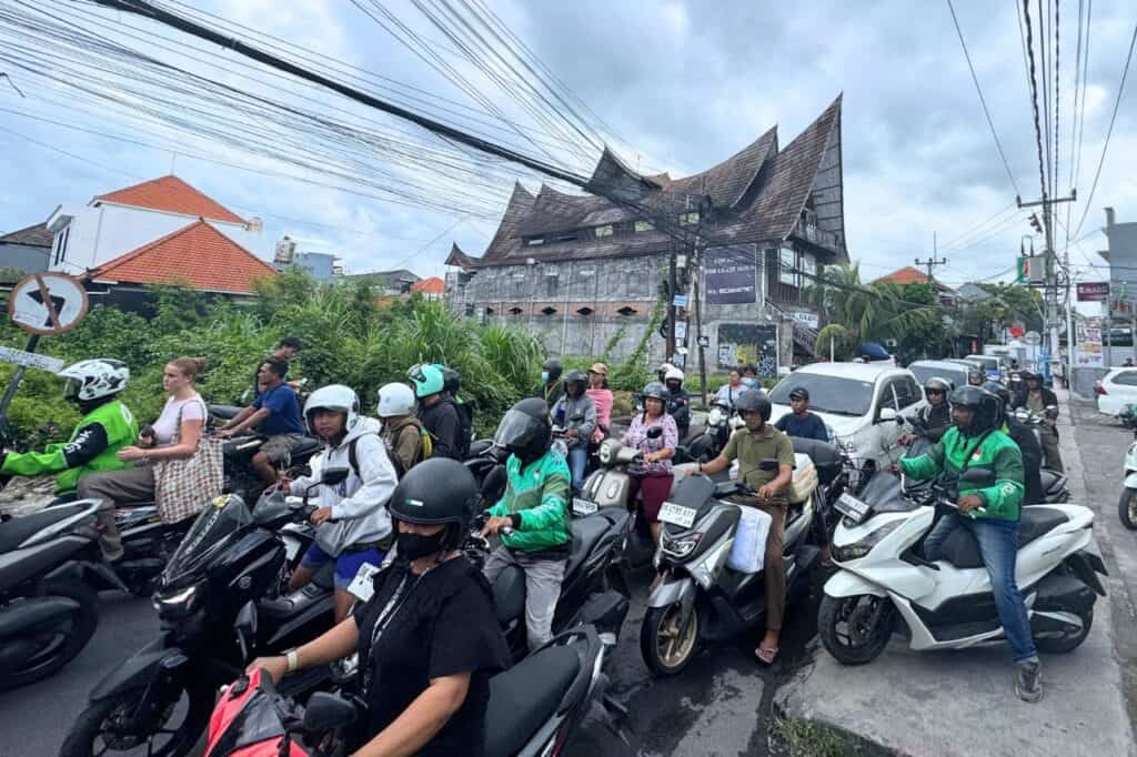 Crowded street in Canggu with dozens of scooters and riders navigating through traffic.