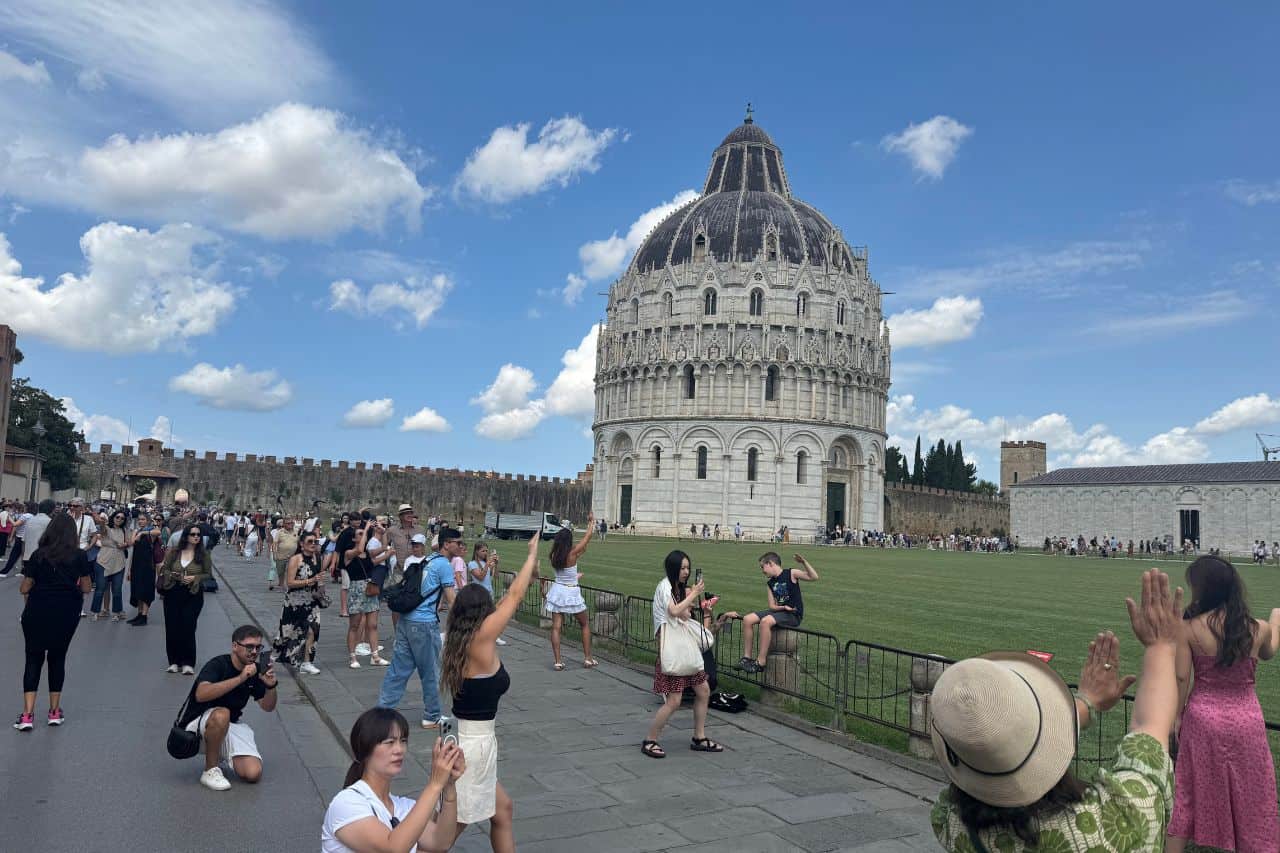 Group of tourists holding their arms up to create the classic Leaning Tower of Pisa photo illusion for their 1 day in Pisa