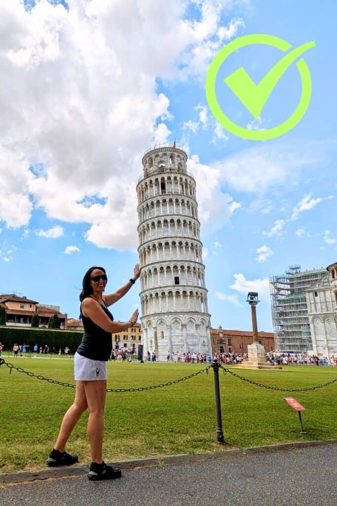 Woman taking a photo of the Leaning Tower of Pisa from an uncrowded grassy area with clear background