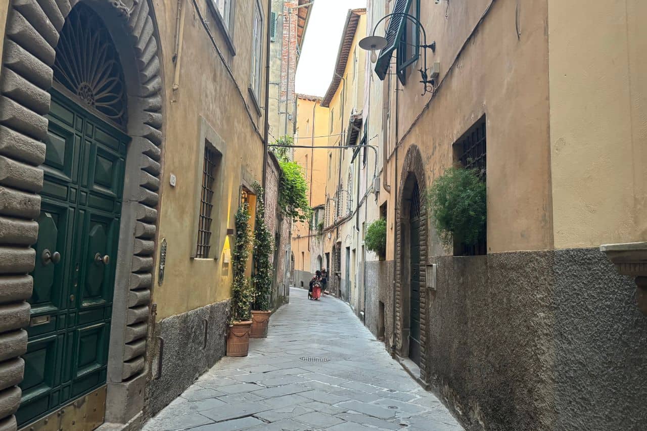 Narrow, quiet side street lined with stone buildings inside the historic center of Lucca Italy