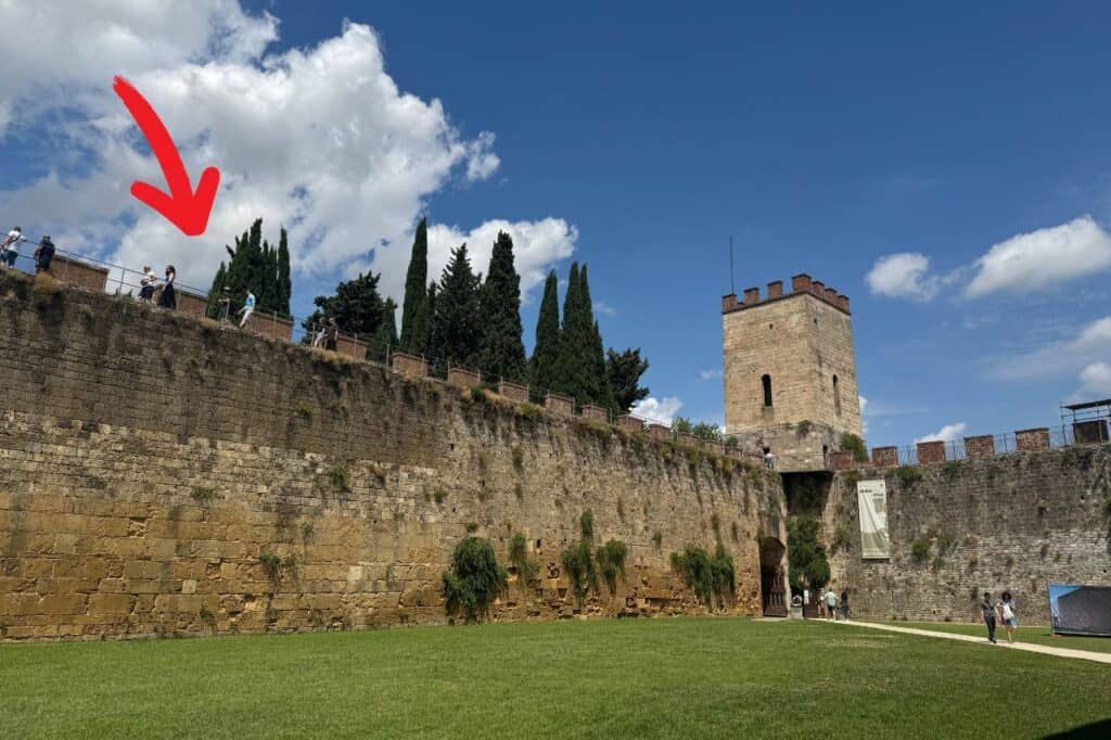 Stone wall in Pisa with directional arrow showing where to access the elevated wall walk near the tower